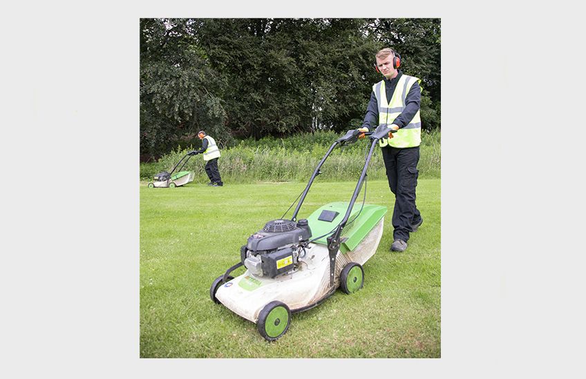 Two people cutting the grass using push lawnmowers