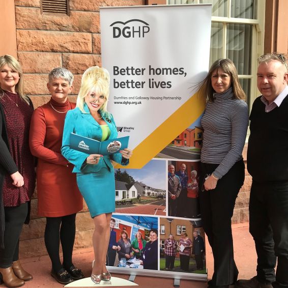 Smiling staff gather around DGHP Better Homes Better Lives banner