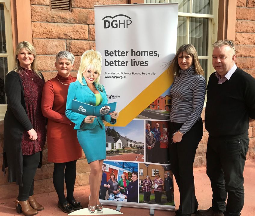Smiling staff gather around DGHP Better Homes Better Lives banner