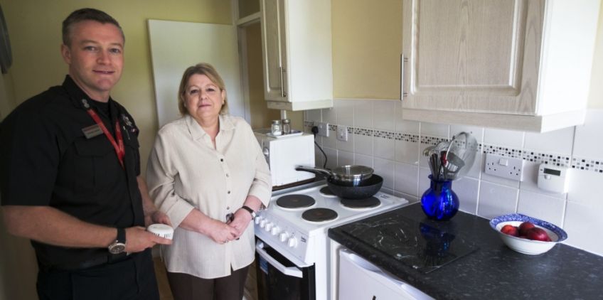 Fire officer with a female standing in her kitchen next to the cooker 